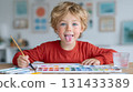 Smiling boy in red shirt painting with watercolor set at home desk 131433389