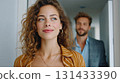 Beautiful young woman standing confidently with man in the background indoors in bright hallway 131433390