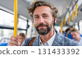 Happy young man standing on city bus while commuting to work using wireless earbuds and smiling at camera 131433392