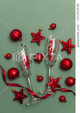 Champagne Flutes with Red Christmas Ornaments and Ribbon on Green Background Champagne Flutes with Red Christmas Ornaments and Ribbon on Green Background 131433416