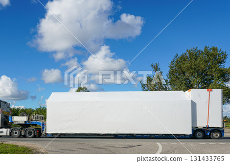Heavy haul truck transporting oversized cargo wrapped in white protective cover on highway Heavy haul truck transporting oversized cargo wrapped in white protective cover on highway 131433765