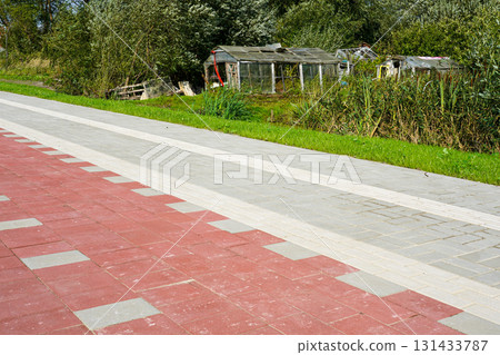 Contrast of new paved sidewalk with old abandoned greenhouses in a rural overgrown landscape 131433787