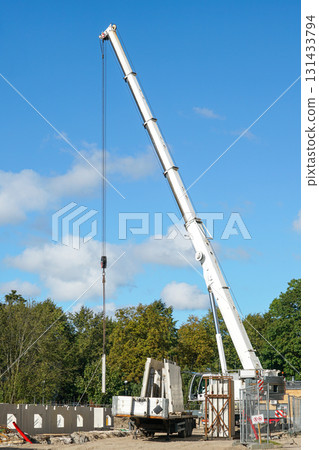 Tall mobile crane lifting prefabricated concrete wall panels at active construction site outdoors Tall mobile crane lifting prefabricated concrete wall panels at active construction site outdoors 131433794