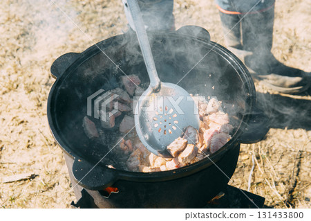 Meat cooking in a large cauldron outdoors over an open fire, a classic outdoor cooking concept for camping and traditional cuisine. 131433800