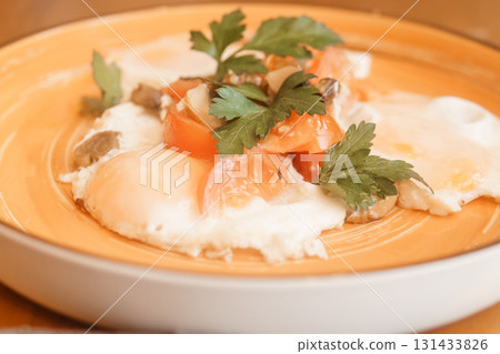 Fried eggs with tomato, mushroom, and parsley served on a plate for a healthy breakfast. Natural and fresh food concept. Fried eggs with tomato, mushroom, and parsley served on a plate for a healthy breakfast. Natural and fresh food concept. 131433826