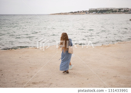 Woman Beach Seaside Coastal Solitude: A lone woman walks a sandy beach, gazing at the calm sea, enjoying solitude near a coastal town, likely for relaxation or contemplation. Woman Beach Seaside Coastal Solitude: A lone woman walks a sandy beach, gazing at the calm sea, enjoying solitude near a coastal town, likely for relaxation or contemplation. 131433991