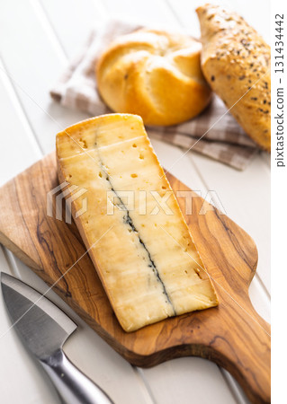 Morbier cheese. Delicious french cheese with mold on cutting board on white table. Morbier cheese. Delicious french cheese with mold on cutting board on white table. 131434442