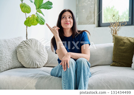 Portrait of beautiful smiling brunette woman sitting on sofa in living room Portrait of beautiful smiling brunette woman sitting on sofa in living room 131434499
