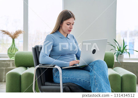 Young woman sitting on chair at home using laptop Young woman sitting on chair at home using laptop 131434512