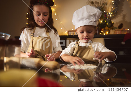 Two Kids Baking Gingerbread Together in Cozy Christmas Kitchen with Aprons and Chef Hat Two Kids Baking Gingerbread Together in Cozy Christmas Kitchen with Aprons and Chef Hat 131434707
