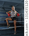 blonde woman dressed in fitness attire shows strength and determination while wearing red boxing gloves. She stands in a boxing ring ready for training. 131435120