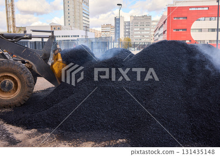 Heavy Machinery Loading Black Aggregate Material at the Construction Site for Development 131435148