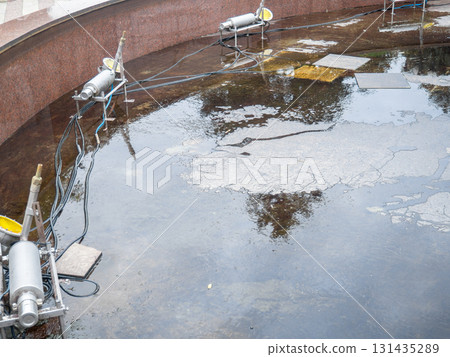 Empty fountain in a city park. Dehumidification. Cleaning the fountain with a hose. The device of the fountain. Pipes for water supply. Water hoses. Modern technologies. 131435289