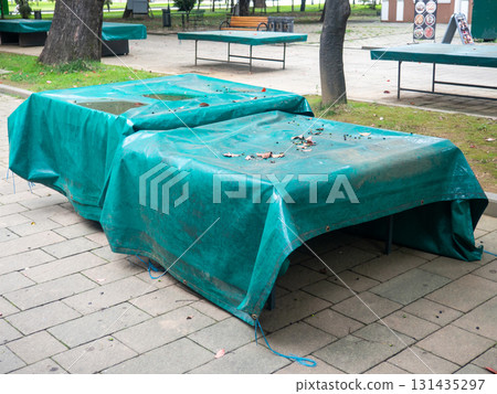 Ping pong tables covered with tarpaulin. Protect mouth from rain. End of summer concept in the park. sport in the park. holiday at the resort. Ping pong tables covered with tarpaulin. Protect mouth from rain. End of summer concept in the park. sport in the park. holiday at the resort. 131435297