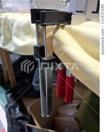 Clamps firmly hold an aluminum corner in a workshop. The setup shows the tools being used for assembly. Various materials and equipment are present around the workspace. Clamps firmly hold an aluminum corner in a workshop. The setup shows the tools being used for assembly. Various materials and equipment are present around the workspace. 131435380