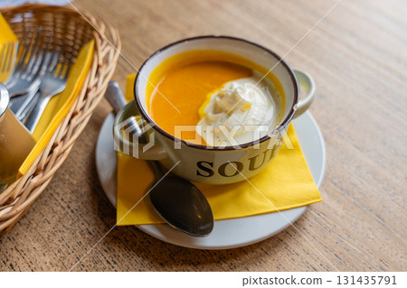 Rustic pumpkin soup served in enamel mug with chipped edge on wooden table. Cottage core 131435791