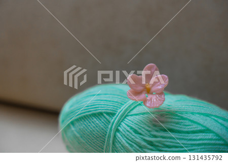 Mint green yarn ball with handmade pink glass flower pin on soft neutral background, copy space 131435792
