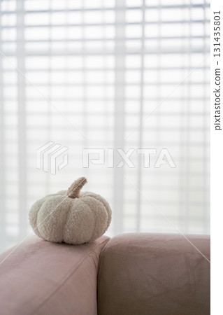 Cozy white fabric pumpkin on pastel sofa with soft light and blurred window blinds background. Cozy white fabric pumpkin on pastel sofa with soft light and blurred window blinds background. 131435801