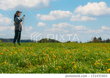 Woman checking phone navigation in spring dandelion meadow in Czech countryside Woman checking phone navigation in spring dandelion meadow in Czech countryside 131435803