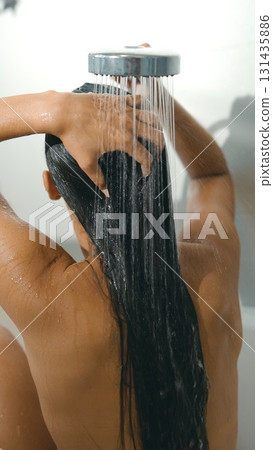 A woman is showering with her long hair flowing beautifully under a soothing waterfall shower 131435886
