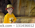 A happy toddler wearing a cap and a yellow tshirt with the word chill and smiling as he plays in the grass under the shade of a tree 131436012