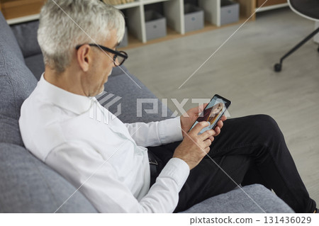 Senior man who's using an online dating app is looking at a photo of a young woman 131436029