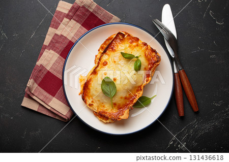 Traditional Italian lasagna on plate with basil garnish on rustic black background top view Traditional Italian lasagna on plate with basil garnish on rustic black background top view 131436618