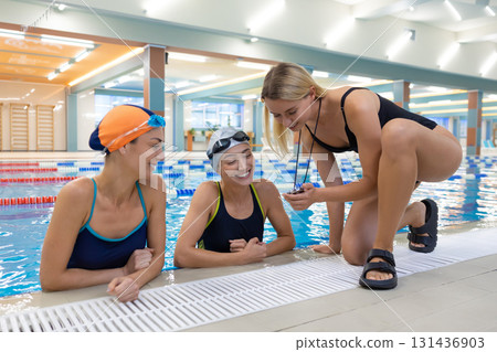 Female swimming coach timing athletes in pool with stopwatch Female swimming coach timing athletes in pool with stopwatch 131436903