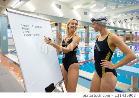Coach with stopwatch teaching swimmer training details on board Coach with stopwatch teaching swimmer training details on board 131436908