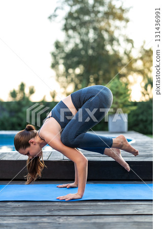 Young long-haired woman standing in bakasana on a yoga mat Young long-haired woman standing in bakasana on a yoga mat 131436991