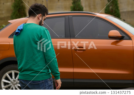 A man meticulously washes and cleans his car in the driveway of his home, showcasing pride in his vehicle and outdoor space. 131437275