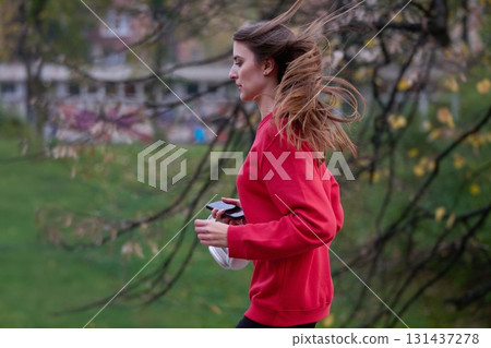 Young beautiful woman running in autumn park and listening to music with headphones on smartphone 131437278