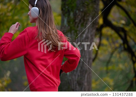 Young beautiful woman running in autumn park and listening to music with headphones on smartphone Young beautiful woman running in autumn park and listening to music with headphones on smartphone 131437288