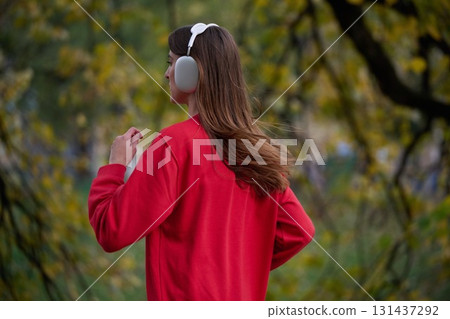 Young beautiful woman running in autumn park and listening to music with headphones on smartphone 131437292
