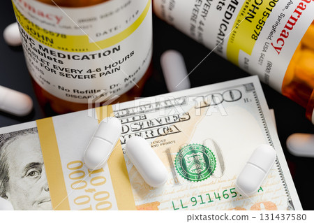 Prescription Medicine Bottles and Pills Next To Stacks of 100 Dollar Bills. 131437580