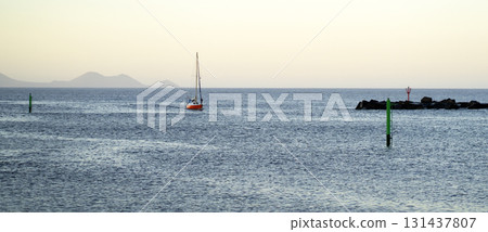 A red yacht sails across the Atlantic Ocean at sunset. A red yacht sails across the Atlantic Ocean at sunset. 131437807