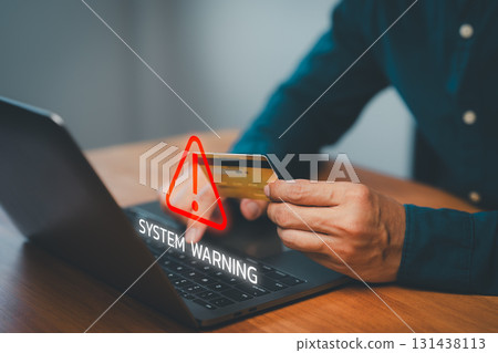 Male hand holding a credit card while using a laptop with warning symbol, representing online payment risk, financial fraud, online shopping and identity theft during digital transactions. Male hand holding a credit card while using a laptop with warning symbol, representing online payment risk, financial fraud, online shopping and identity theft during digital transactions. 131438113