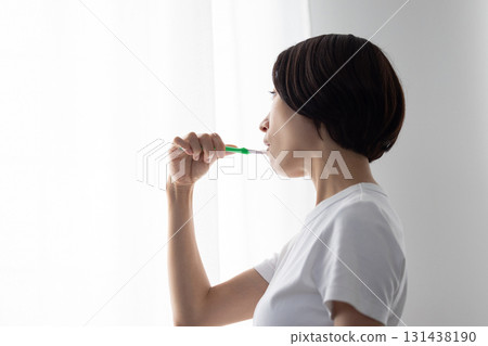 Middle-aged woman brushing her teeth by the window 131438190
