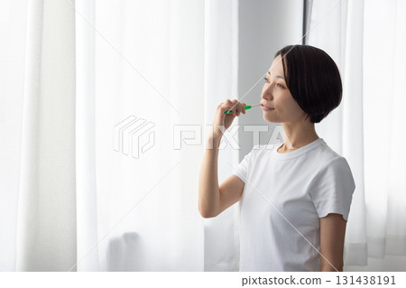 Middle-aged woman brushing her teeth by the window 131438191