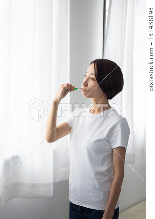Middle-aged woman brushing her teeth by the window 131438193