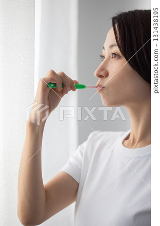 Middle-aged woman brushing her teeth by the window 131438195