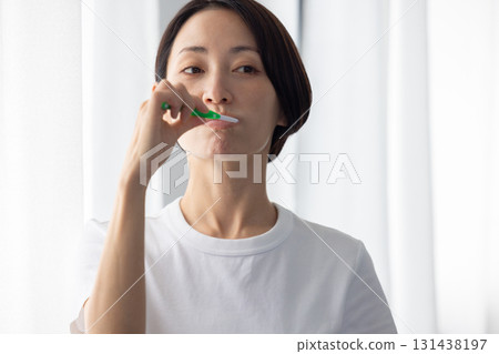 Middle-aged woman brushing her teeth by the window 131438197