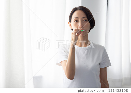 Middle-aged woman brushing her teeth by the window Middle-aged woman brushing her teeth by the window 131438198