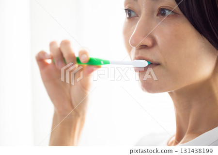 Middle-aged woman brushing her teeth by the window Middle-aged woman brushing her teeth by the window 131438199