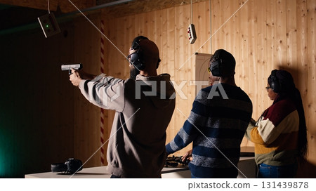 Friends in firing range doing recreational shooting, pressing mechanism to recall paper targets. People training with handguns, sharpening skills, checking points scored on bullseyes, camera A 131439878