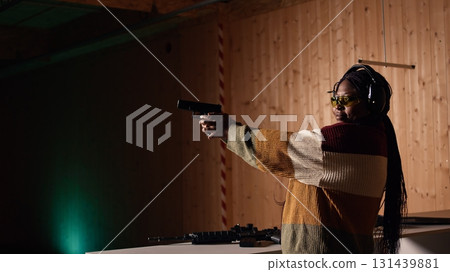 Person wearing safety equipment loading bullets cartridge in pistol during firearm practice session at shooting range. Woman reloading gun, pointing weapon at targets, learning self defense, camera A 131439881