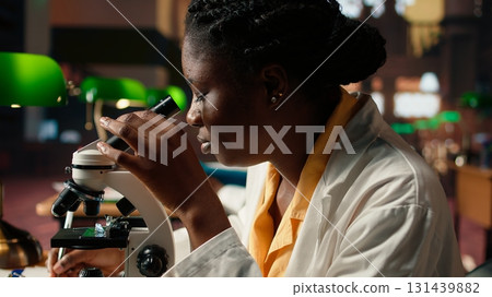 Future researcher works on her thesis by examining microorganisms under the microscope lenses, reading about microbiology and medical science. Focus on scientific exams. Close up. Camera A. Future researcher works on her thesis by examining microorganisms under the microscope lenses, reading about microbiology and medical science. Focus on scientific exams. Close up. Camera A. 131439882
