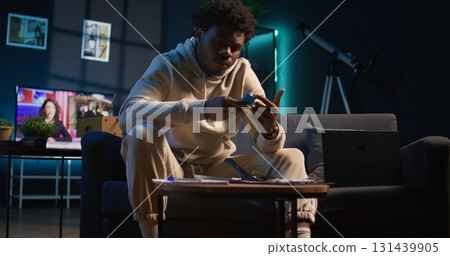 Black remote worker suffers from diabetes and uses glucometer at home, checking his sugar levels with a blood sample. Young adult using an insulin pen for glucose measurement. Camera B. Black remote worker suffers from diabetes and uses glucometer at home, checking his sugar levels with a blood sample. Young adult using an insulin pen for glucose measurement. Camera B. 131439905