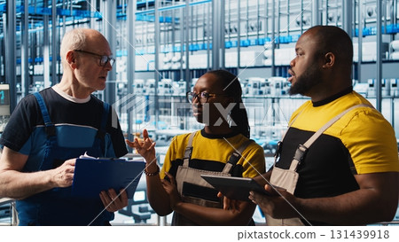Smart factory team leader teaching new trainees to test automated systems and ensure reliability. Senior engineer doing induction to intern, training them to identify bottlenecks, camera A 131439918