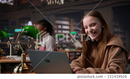 Diverse classmates sharing high five and feeling happy with their success, finishing school assignment in time and expecting a high grade. Girls doing amazing teamwork at the library. Camera B. 131439926